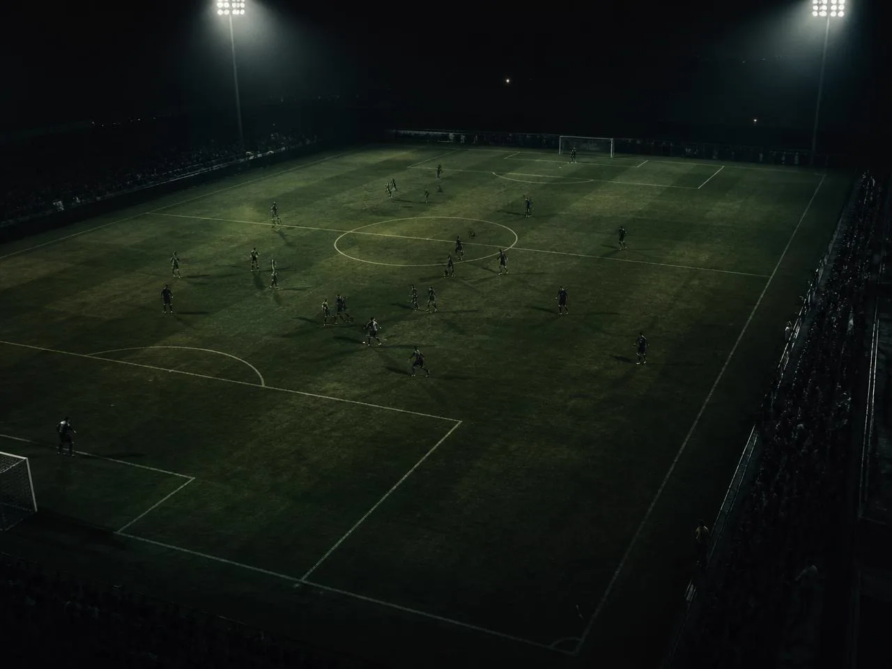 Floodlit football pitch with professional players in dark kits